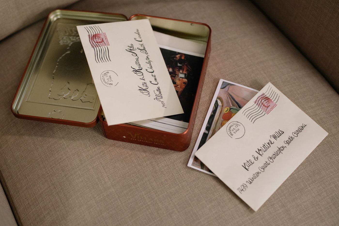 A vintage tin of envelopes and postcards resting on a sofa