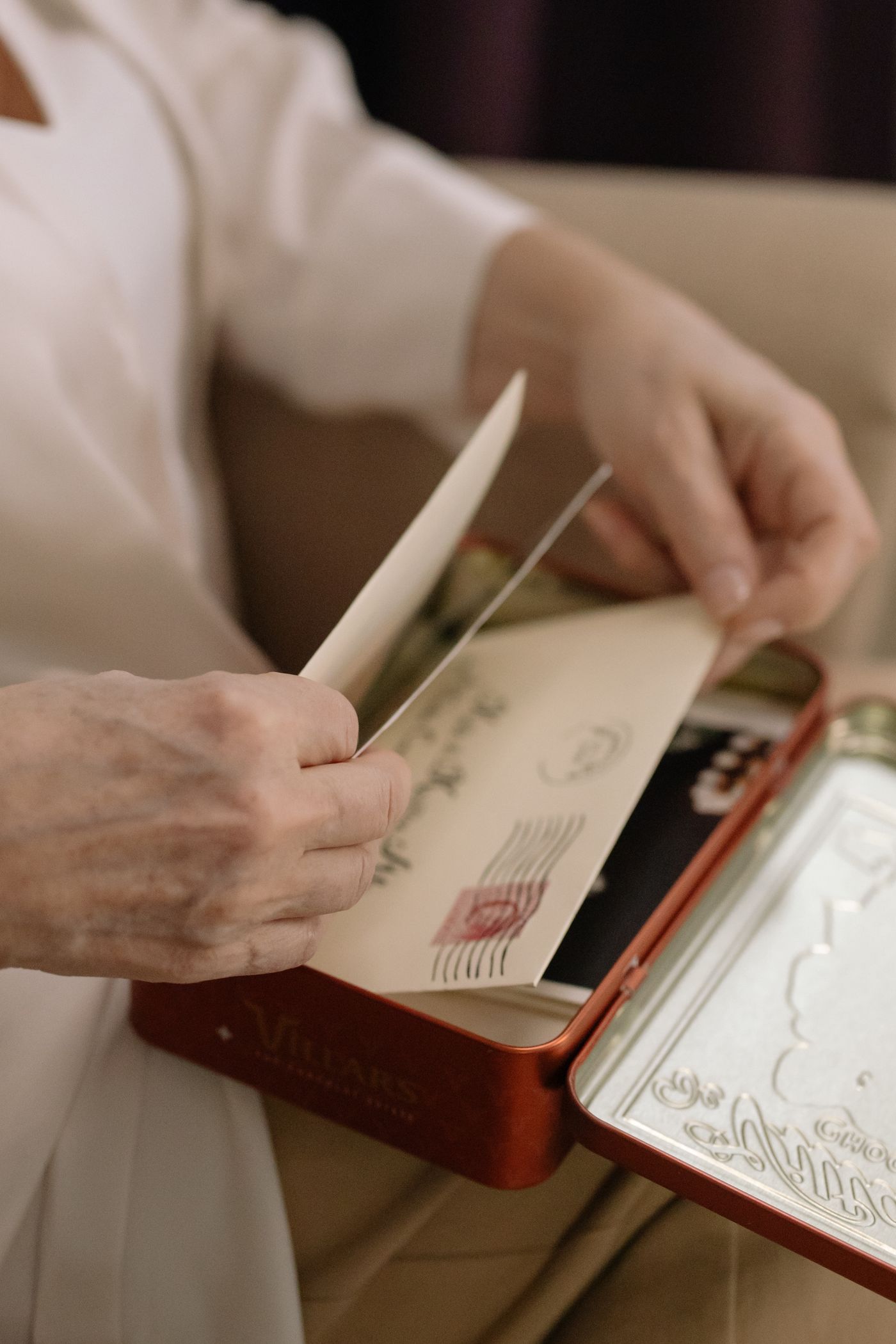 Hands lifting an old letter out of a red keepsake tin